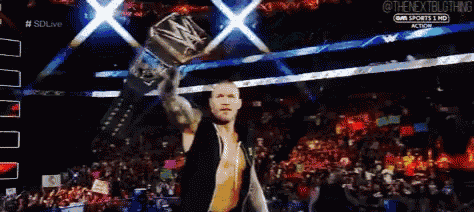 a man in a black vest is holding a wrestling championship belt in front of a crowd