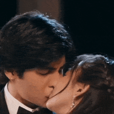 a man in a tuxedo and a woman in a dress are kissing each other .