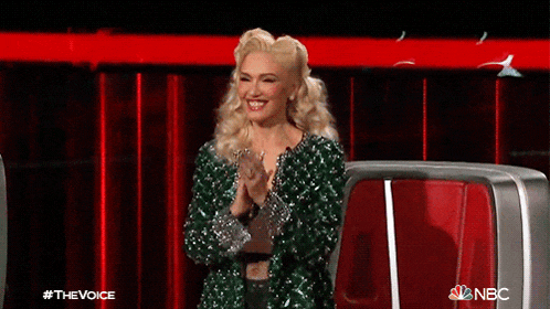 a woman in a green sequined jacket applauds while sitting in front of a nbc logo