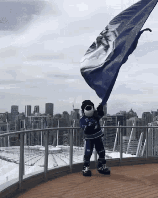 a mascot holding a blue and white flag with the letter t on it