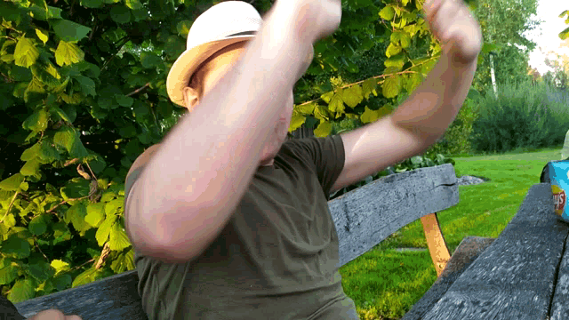 a man wearing a hat is sitting on a bench with a bag of potato chips next to him