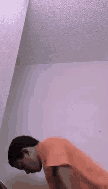a man in an orange shirt is standing in a room with his head down .