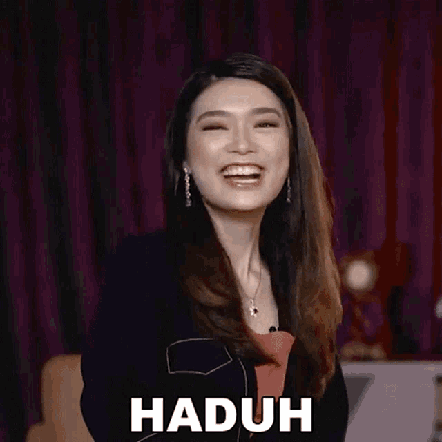 a woman is smiling and clapping her hands in front of a purple curtain while wearing earrings .
