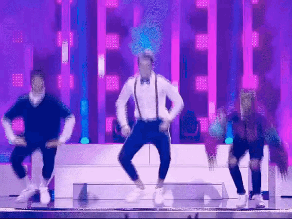 a group of people are dancing on a stage with purple lights