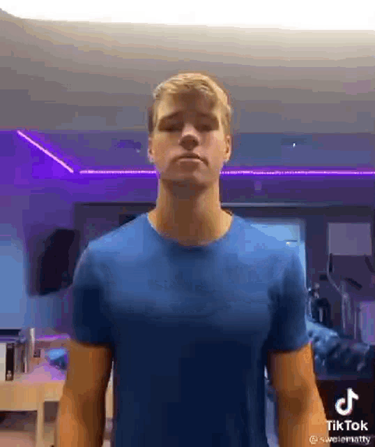 a young man in a blue shirt is standing in a room with purple lights .