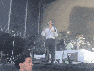 a man in a white shirt singing into a microphone on a stage