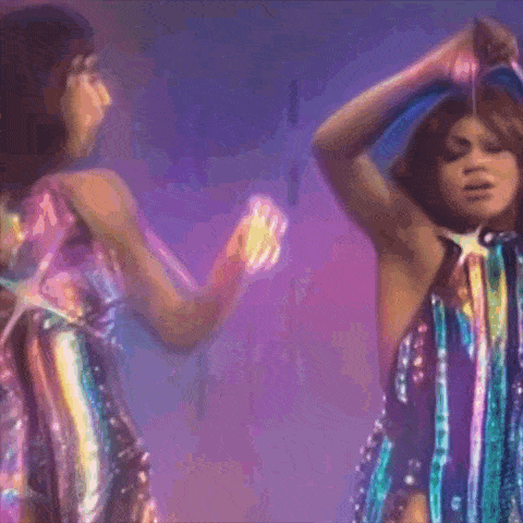 two women in colorful dresses are dancing on a stage in front of a purple background