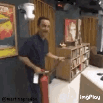 a man is holding a fire extinguisher in a room with a bookshelf in the background .