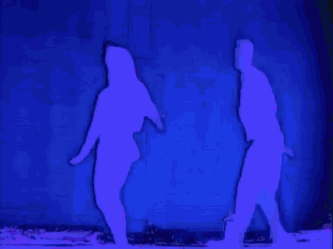 a silhouette of a man and a woman dancing in front of a blue wall .