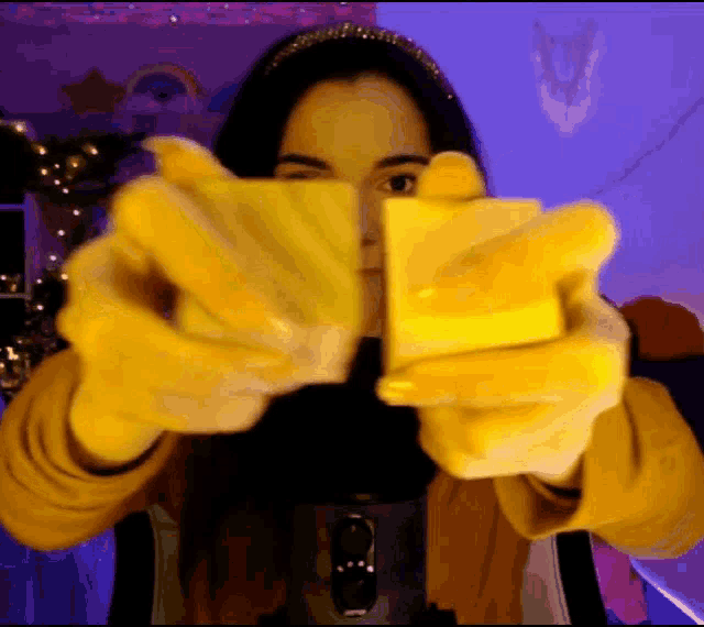a woman wearing yellow gloves is holding a yellow block in front of her face