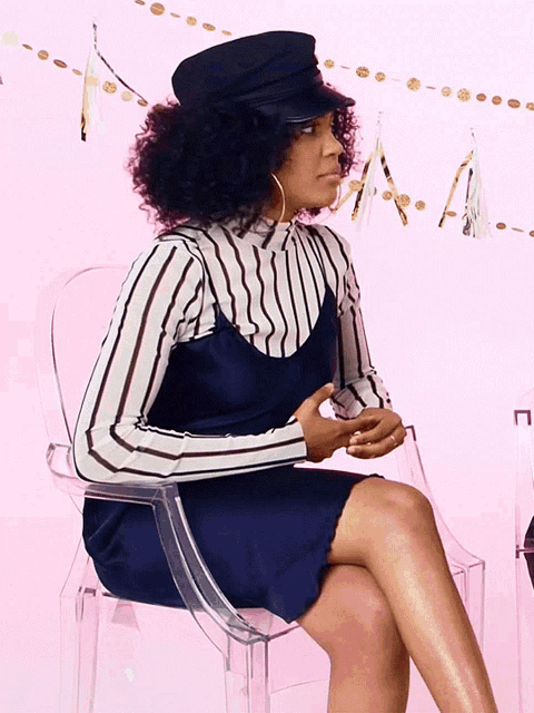 a woman wearing a black hat and a striped top sits in a clear chair