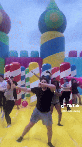 a group of people are dancing in front of a bouncy house that says tik tok on it