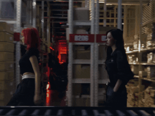 two women are walking in a warehouse with a red sign that says 5205