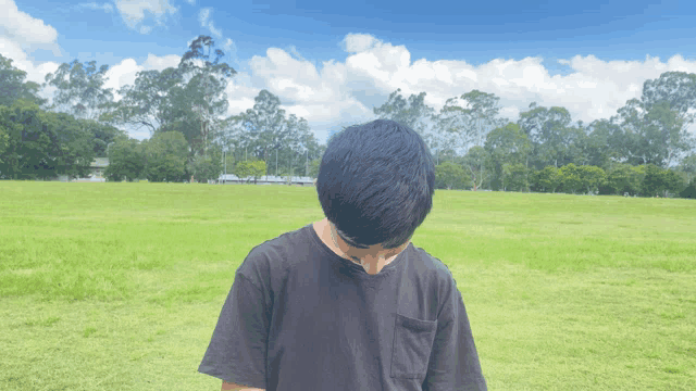 a man in a black shirt stands in a grassy field with his head down