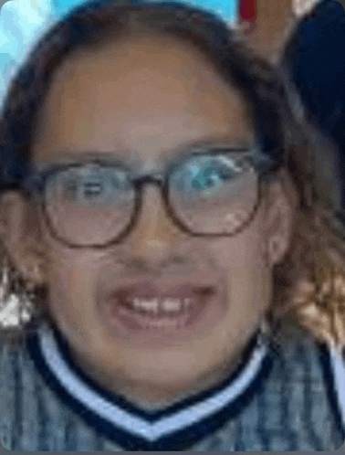 a young girl wearing glasses and a sweater is smiling and making a funny face .