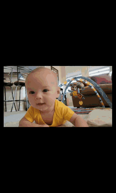 a baby in a yellow shirt is smiling and crawling on the floor