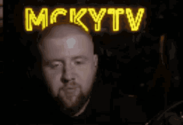 a man with a beard stands in front of a neon sign that says mckytv