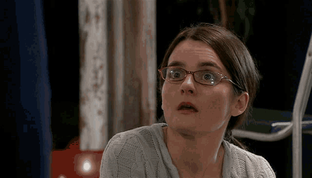 a woman wearing glasses and a grey sweater is making a surprised face