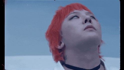 a man with red hair and a choker looks up into the sky