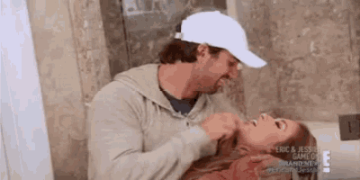 a man in a white hat is holding a woman 's neck .