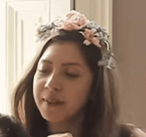 a woman wearing a flower crown on her head is holding a black cat .