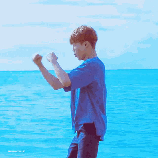 a man in a blue shirt is standing in front of a body of water ..