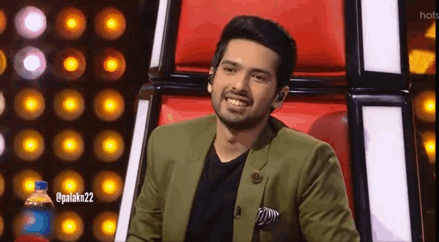 a man in a green suit is sitting in a red chair and smiling .