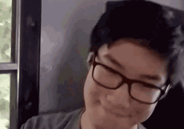 a young man wearing glasses is smiling while sitting in front of a window .