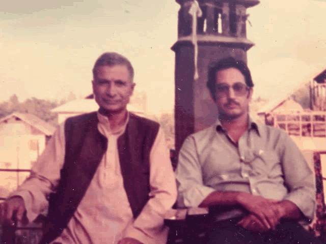 two men sitting next to each other in front of a building