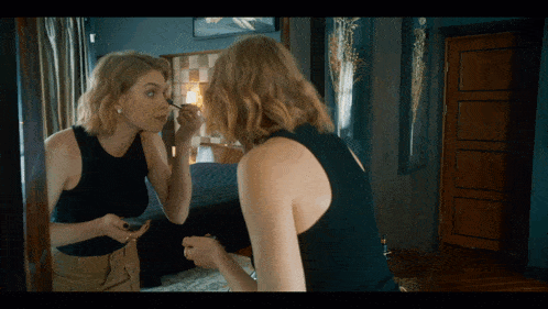 a woman in a black tank top is applying mascara to her eye