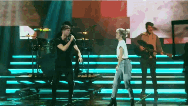 a man is singing into a microphone while a woman stands next to him on stage .