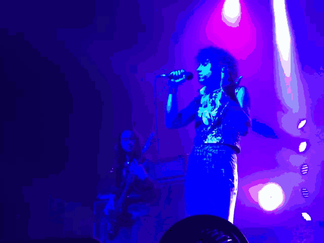 a woman singing into a microphone on a stage with purple lights behind her