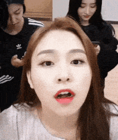 a woman with red lipstick on her lips is making a funny face while two other women look on .