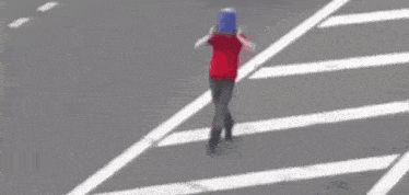 a person wearing a blue bucket on their head is crossing the street .