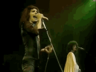 a woman is singing into a microphone on a stage while a man plays a guitar .