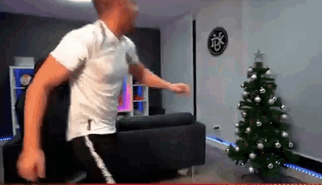 a man in a white shirt is dancing in a living room with a christmas tree in the background .