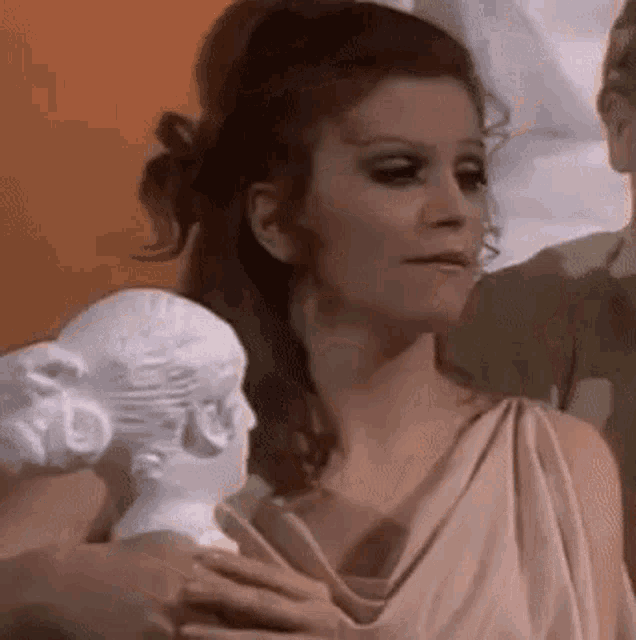 a woman in a toga is holding a statue of a woman 's head .