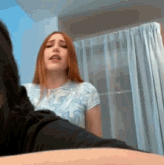 a woman with red hair is sitting in front of a window with curtains