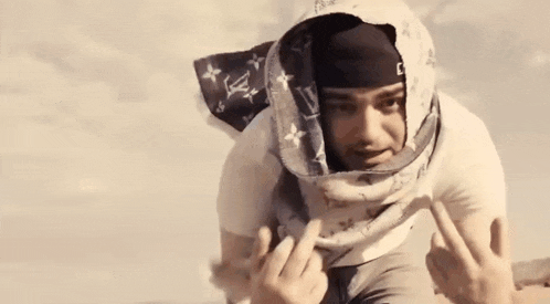 a man wearing a scarf around his head and a bandana is giving the middle finger .