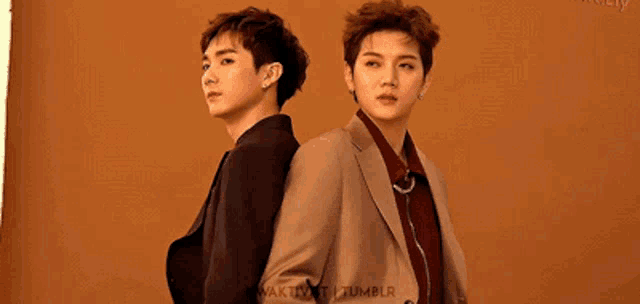 two young men in suits are standing back to back and looking at the camera .
