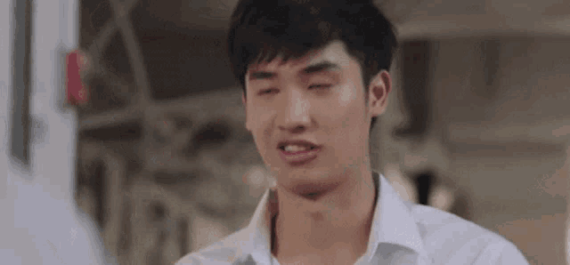 a young man in a white shirt is making a funny face while standing in a room .