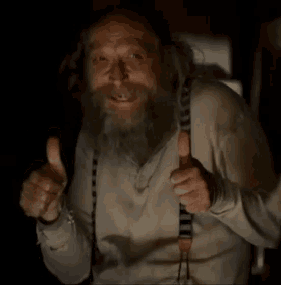 a man with a beard wearing suspenders gives a thumbs up