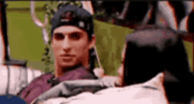 a man wearing a baseball cap is sitting on a couch looking at a woman .