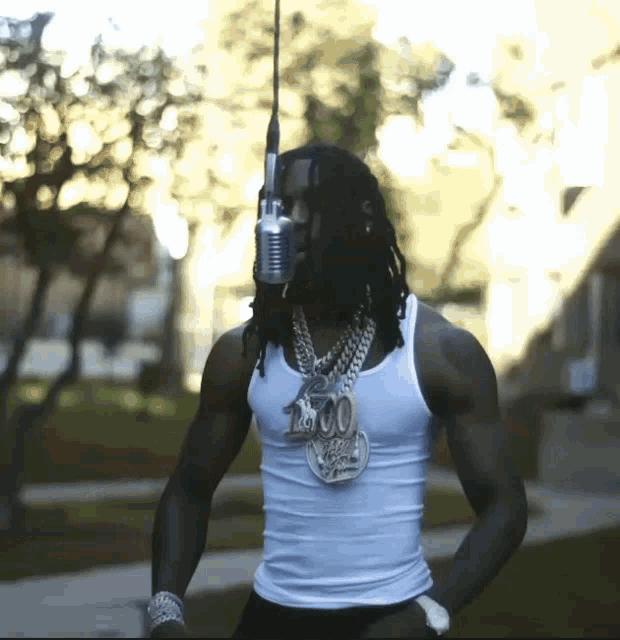 a man with dreadlocks is wearing a white tank top and a necklace with the number 1000 on it