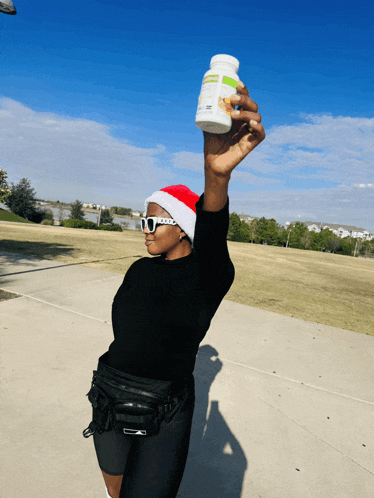 a woman wearing a santa hat is holding up a bottle of vitamins