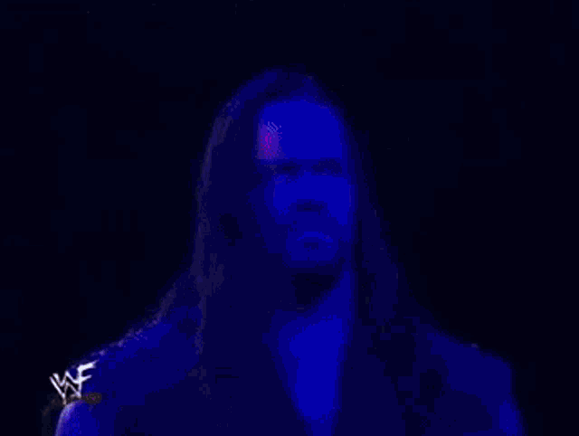 a man with long purple hair and a beard is wearing a purple shirt and has glowing eyes .