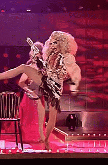 a drag queen is holding a gun and kicking her leg
