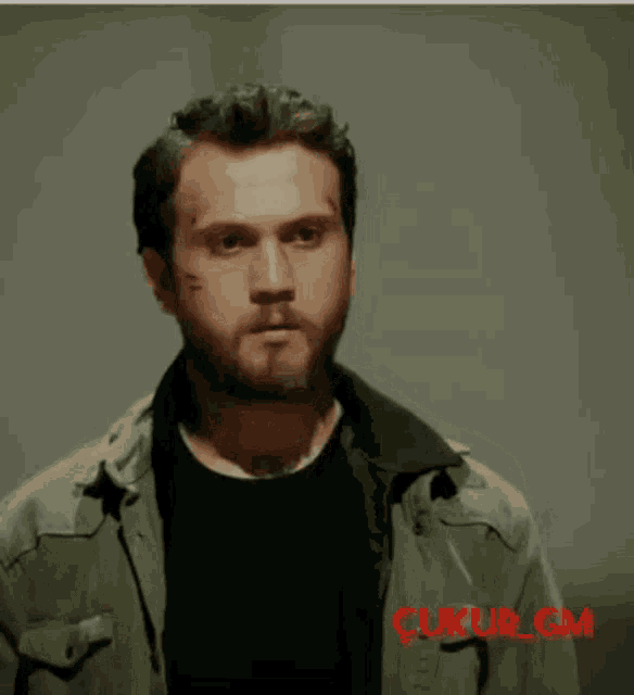 a man wearing a green jacket and a black shirt has the word cukur on the bottom of his shirt