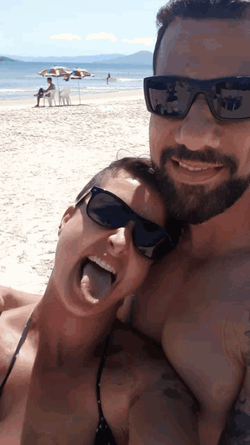 a man and woman are posing for a picture on the beach and the woman is sticking her tongue out