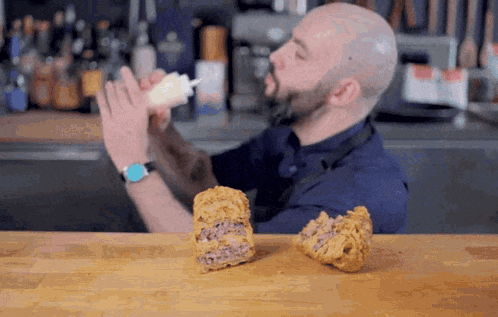 a bald man with a beard is pouring sauce on a fried food